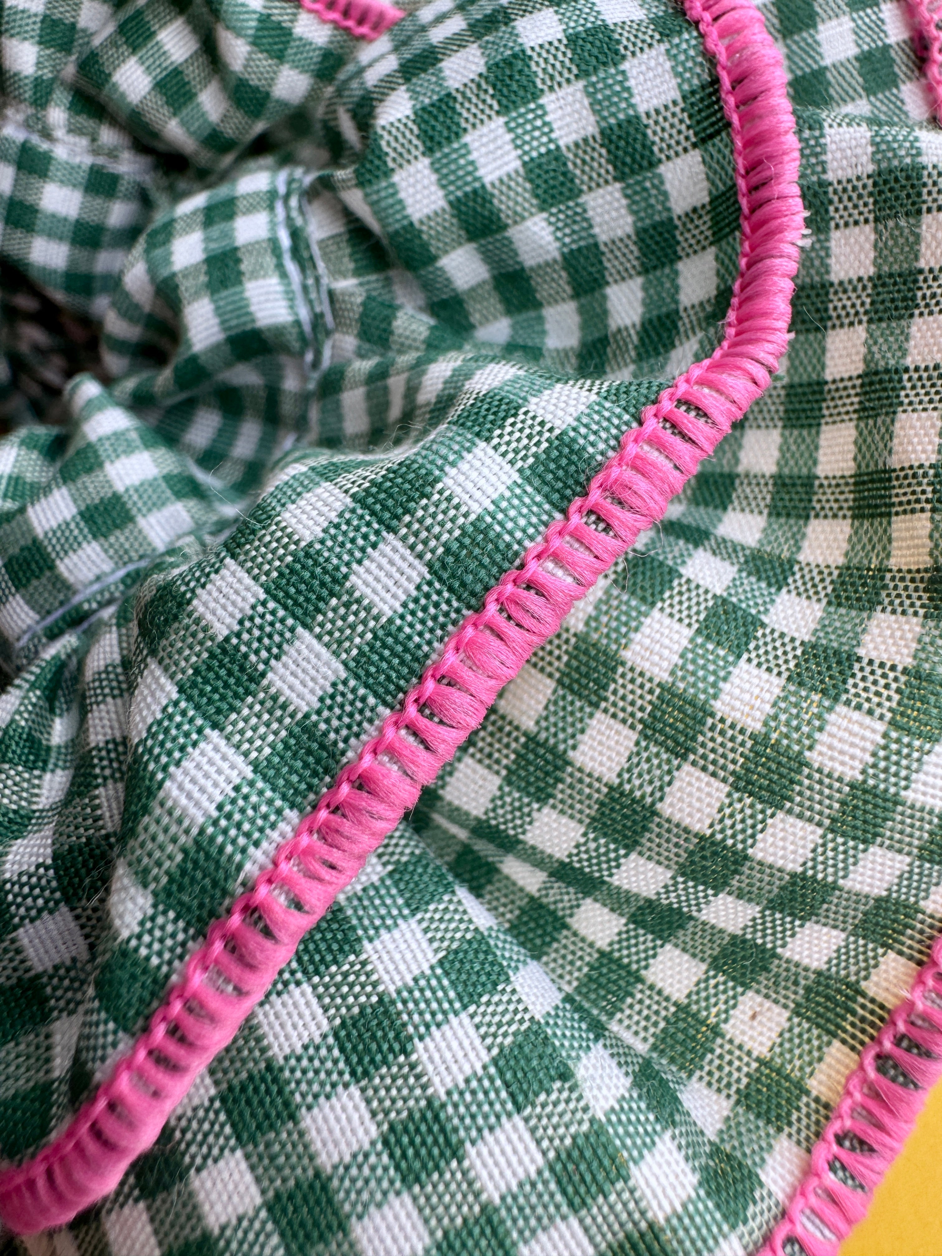 Close-up of a green and white gingham checkered fabric with a prominent pink stitched border.