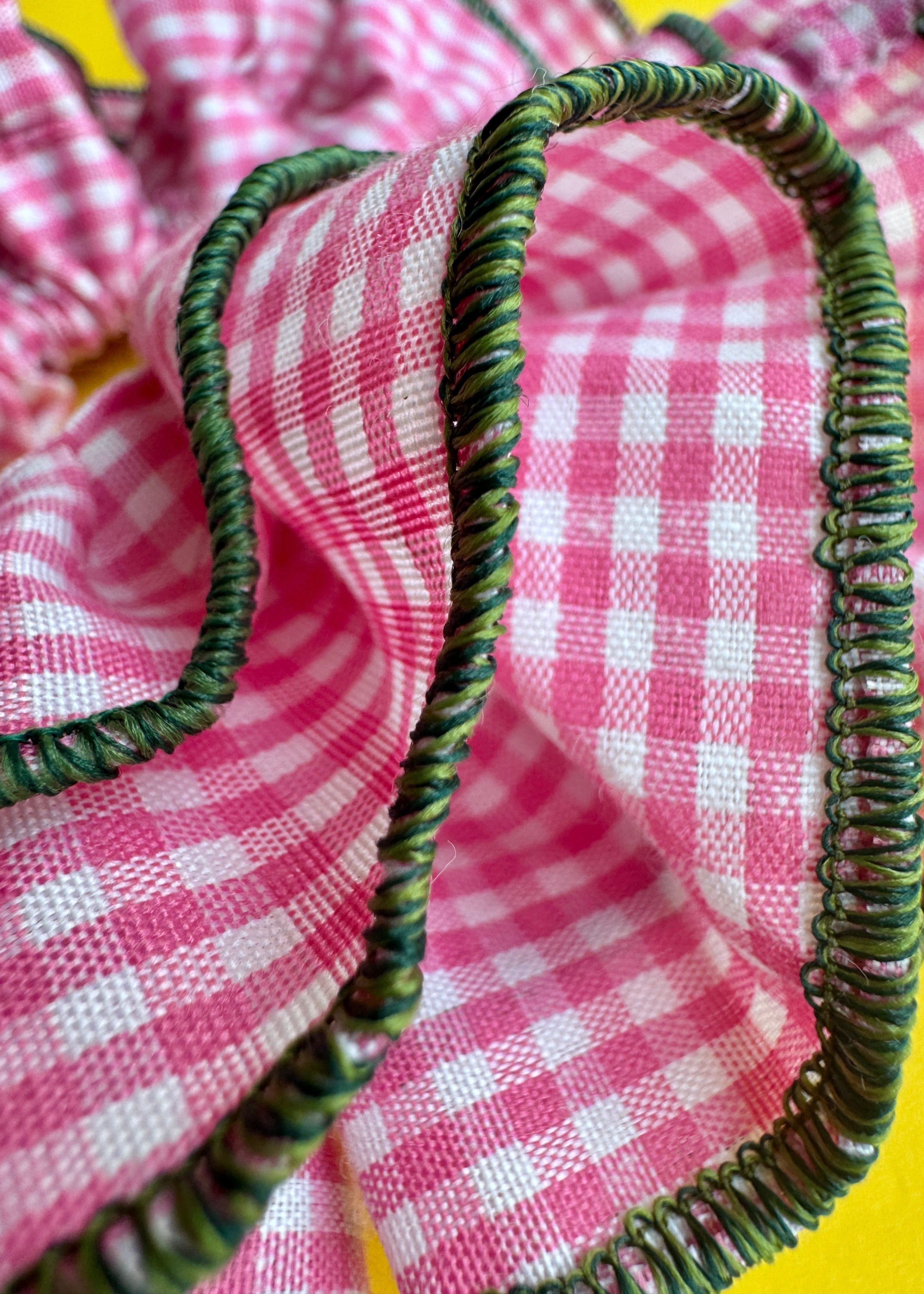 A close-up of a pink and white gingham fabric trim with a thick, twisted dark green border.