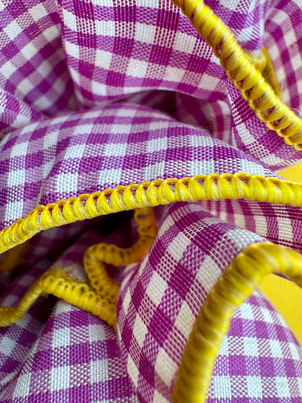 Close-up of a purple and white gingham checkered fabric with bright yellow braided trim.