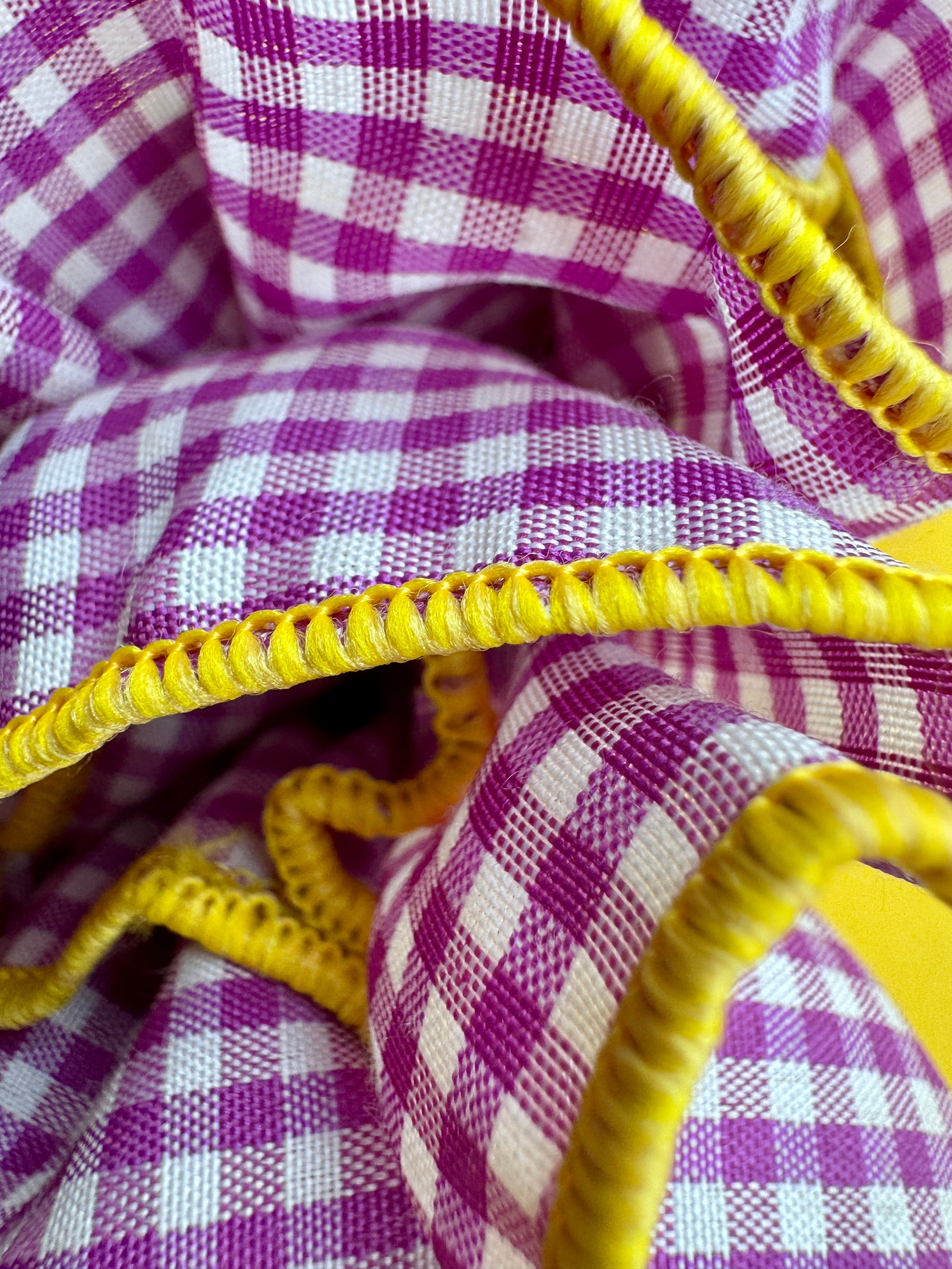 Close-up of a purple and white gingham checkered fabric with bright yellow braided trim.