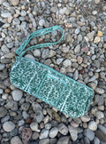 A mint green and white patterned woven wristlet clutch with a matching wrist strap, laid flat on a bed of small gray and beige pebbles.